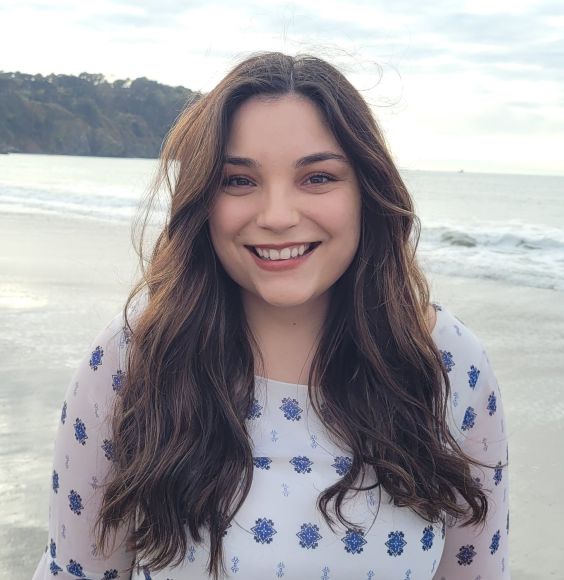 Headshot of Jessica Mangili smiling and standing in front of a beach landscape.