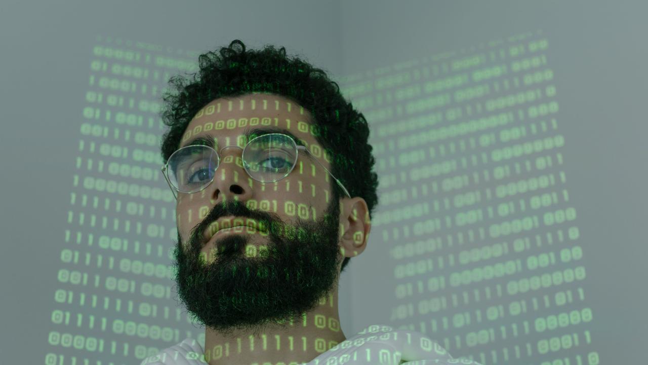 Man with glasses. Ones and zeros, like binary code, are projected onto his face.