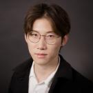 Headshot of Assistant Professor Junwen Hu, with glasses, white shirt and black jacket on dark gray background